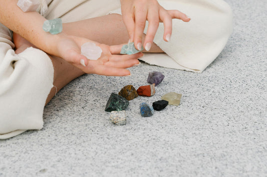 Close-up of a person holding various colorful crystals, including amethyst, citrine, and rose quartz, arranged on a granite surface.