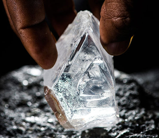 Close-up of a person holding a large, clear crystal with a distinct triangular shape, displayed against a dark background.