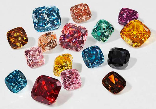Collection of colorful gemstones including blue, pink, yellow, green, red, and black diamonds arranged in various shapes on a white background.