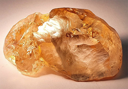 Close-up of a large, rough yellow gemstone with a smooth surface and subtle reflective shine, showcasing its natural crystal structure and vibrant color.