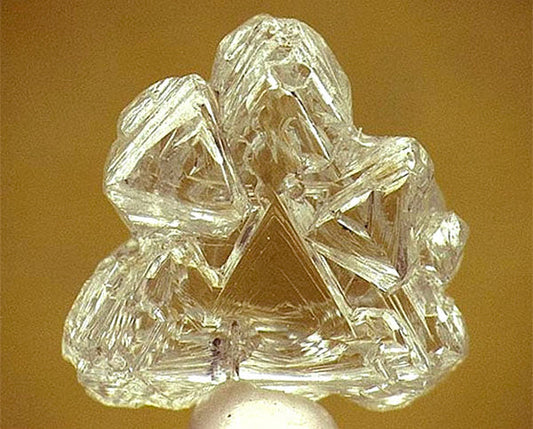 Close-up of a rough, uncut diamond with a unique and intricate crystal structure. The diamond displays natural facets and sharp edges, showcasing its raw form before being polished.