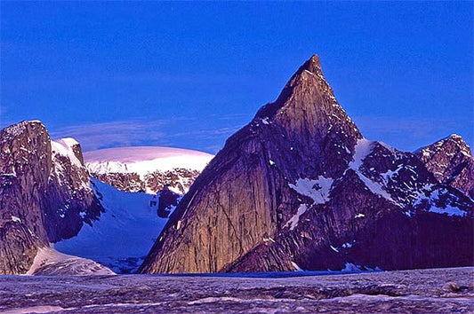Majestic mountain peak in the Arctic region with snow-covered slopes and glaciers, set against a blue sky during twilight.