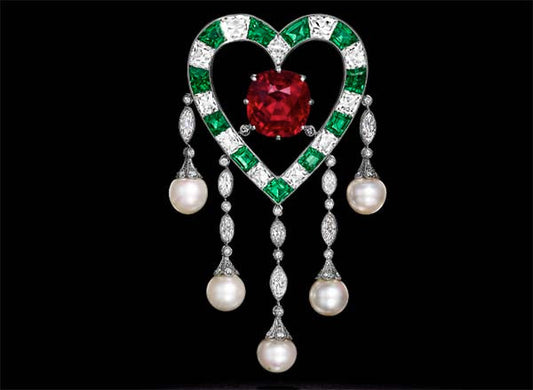 Elegant heart-shaped jewelry featuring a large red ruby in the center, surrounded by green emeralds and diamonds, with pearl drops.