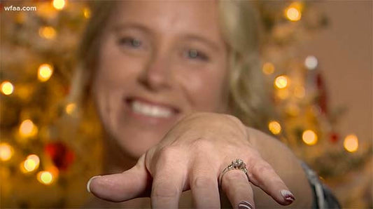 Smiling woman with a diamond engagement ring on her hand in front of a Christmas tree, with a soft blurred background.