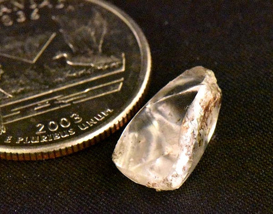 Close-up of a rough diamond next to a quarter coin, highlighting its crystal structure and size comparison, showcasing the raw, uncut form of the gemstone.