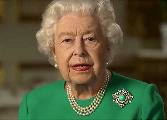 Queen Elizabeth II wearing a green outfit with a pearl necklace and a brooch, speaking to the camera in a formal setting.