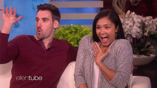 Couple on the Ellen show expressing excitement and surprise with wide smiles and raised hands, sitting together on a couch.