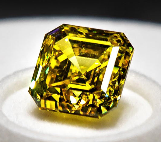 Close-up image of a vibrant yellow diamond with an emerald cut, showcasing its brilliance and clarity, placed on a white surface.