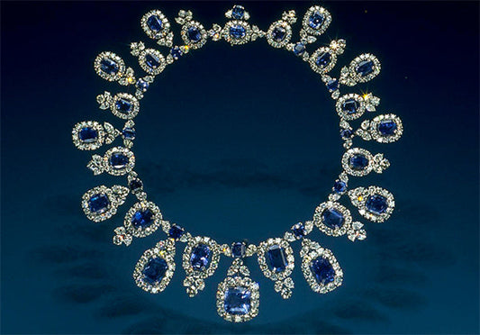 Close-up of an elegant sapphire and diamond necklace featuring a series of oval and cushion-cut sapphires, surrounded by sparkling diamonds. The necklace is set against a dark background, highlighting the luxurious design and fine craftsmanship.