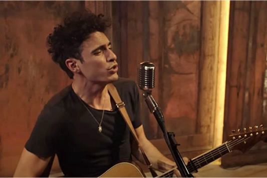 Male musician performing with guitar and microphone, singing passionately.