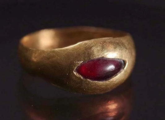 Close-up of a vintage gold ring with a marquise-shaped red gemstone set in the center.