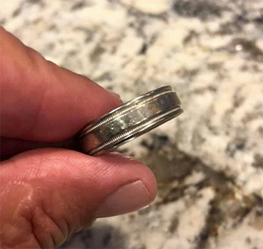 Close-up of a person holding a silver wedding ring with intricate detailing, displayed on a marble surface.