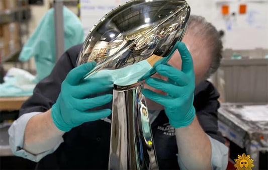 Close-up of a worker polishing the iconic Super Bowl trophy, wearing protective gloves in a manufacturing facility.