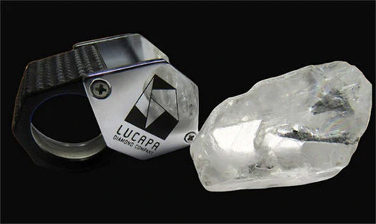 Close-up of a Lucapa Diamond Company diamond ring with a rough, uncut diamond beside it on a black background.