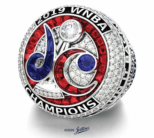 Close-up of the 2019 WNBA Championship ring, featuring intricate designs with red, blue, and white gemstones, and the 'DC' logo surrounded by sparkling diamonds, commemorating the team's victory.