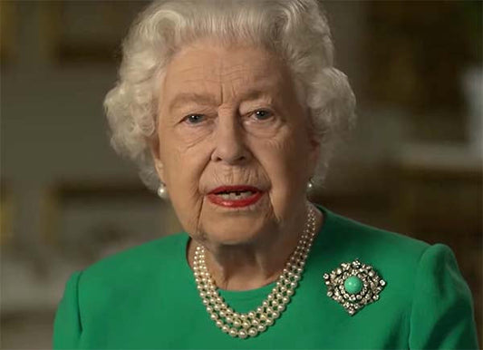Queen Elizabeth II wearing a green outfit with a pearl necklace and a brooch, giving a speech.