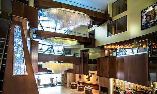 Modern luxury interior featuring a grand staircase with glass railings and intricate crystal chandeliers, surrounded by elegant wood paneling and spacious living areas.