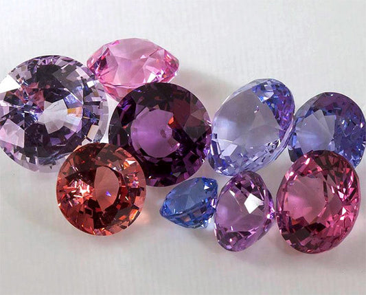 Collection of vibrant purple and pink gemstones, including various cuts like round and oval, showcasing their brilliant sparkle and high-quality clarity, ideal for jewelry design.