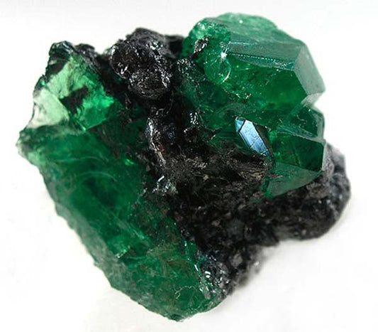 Close-up view of a rough emerald crystal with vibrant green color, partially embedded in dark rock, highlighting the natural facets and texture of the gem.