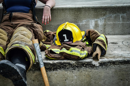 Firefighter gear resting on concrete steps: yellow helmet with '1' badge, firefighter jacket and pants, and axe.
