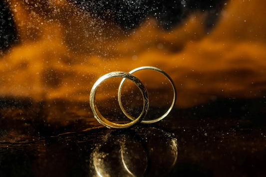 Close-up of two gold wedding bands with intricate engravings, reflecting light against a dark, blurred background.