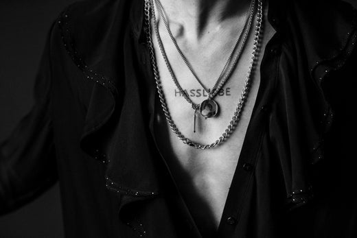 Close-up of a person wearing layered necklaces with a pendant and a tattoo on the chest.