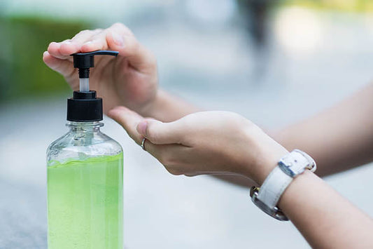 Close-up of a person using a pump dispenser to apply green liquid soap or hand wash.