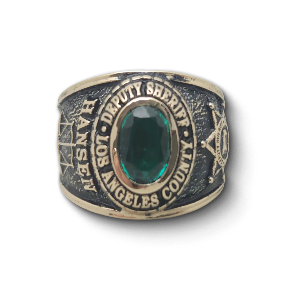Close-up of a Deputy Sheriff Los Angeles County ring, featuring a large emerald gemstone at the center, with detailed engravings and sheriff insignia on the band.