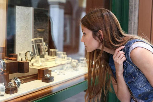Young woman admiring luxury watches in a store display window, with a focus on the watch collection.