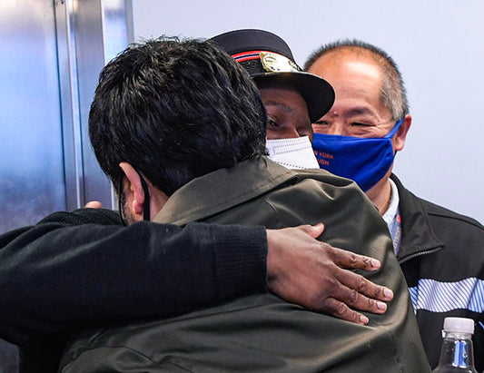 Emotional moment of three people hugging, with two men in uniforms and a third person wearing a mask, sharing a heartfelt embrace.