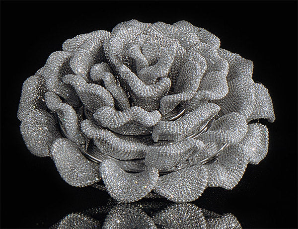 A sparkling diamond-encrusted brooch shaped like a rose, displayed against a black background.