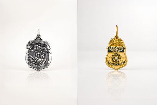 Silver Saint Michael and gold U.S. Customs Special Agent badge pendants displayed side by side on a white background with reflections.