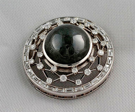 Vintage brooch featuring a large black cabochon gemstone at the center, surrounded by a halo of round and baguette diamonds set in intricate silver web design.