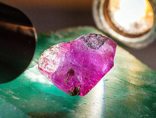 Close-up image of a raw pink ruby gemstone illuminated by light, showing its natural facets and imperfections.