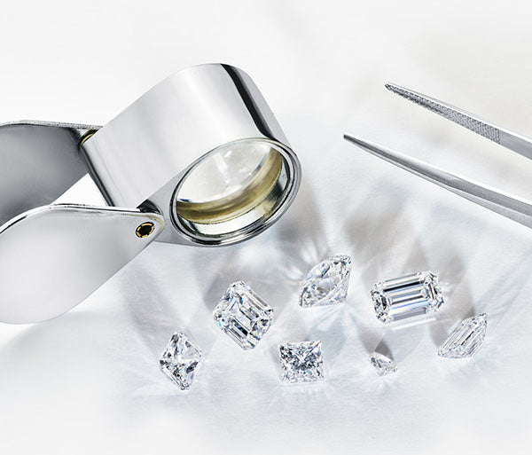 Close-up of a jeweler's loupe and tweezers next to several loose, polished diamonds with various cuts, showcasing the clarity and quality of each stone.