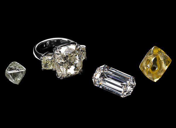 A collection of luxury diamonds including a large cushion-cut diamond ring, rectangular diamonds, and a yellow diamond, displayed on a black background.
