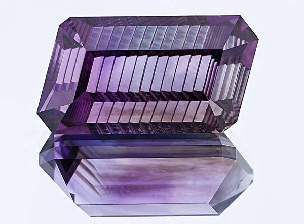 Close-up image of a purple amethyst crystal with sharp geometric facets, reflecting light on a flat surface.