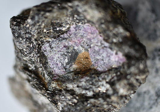 Close-up of a rough mineral rock featuring visible purple and grayish crystals, showcasing its raw texture and natural formation.