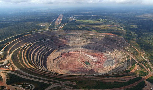 Aerial view of an open-pit mining site with multiple layers of excavation, revealing a large, circular pit surrounded by roads and vegetation.