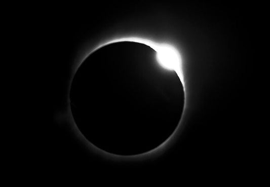 Stunning view of a solar eclipse with the sun's corona glowing around the darkened moon, captured in high contrast against a dark sky.