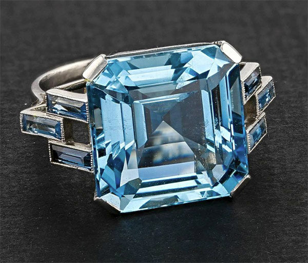 Elegant silver ring featuring a large square-cut blue topaz gemstone with smaller blue accents on the band.