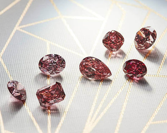 A collection of seven pink diamonds in various shapes including oval, pear, and cushion, arranged on a geometric-patterned surface.