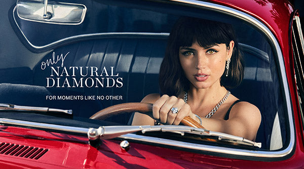 Young woman driving a red vintage car, wearing diamond jewelry with a close-up view of her ring and necklace. The image features the text 'Only Natural Diamonds For Moments Like No Other.