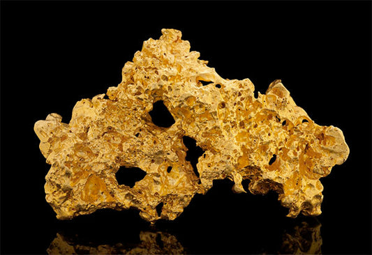 Close-up of a natural gold nugget with rough texture and multiple cavities, displayed against a black background.