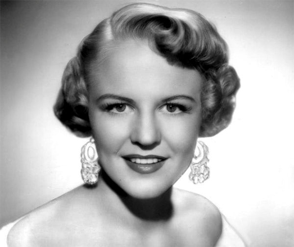 Black and white portrait of a woman with vintage curled hairstyle, wearing large dangling earrings and a slight smile.