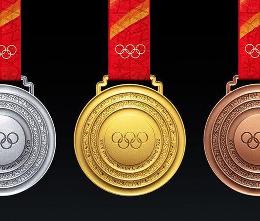 Gold, silver, and bronze Olympic Winter Games 2022 medals displayed on black background with red and gold ribbons.