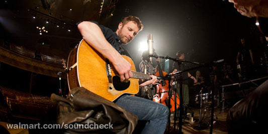 Musician playing an acoustic guitar during a live soundcheck performance on stage with a band.