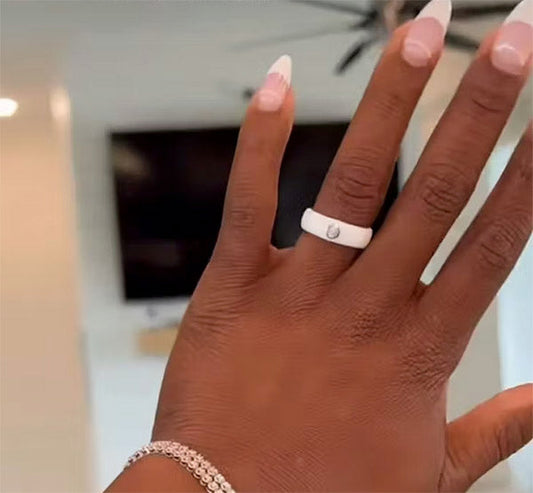 Close-up of a hand wearing a sleek white ring and a diamond bracelet, with elegant French-tipped nails, in a modern home setting.