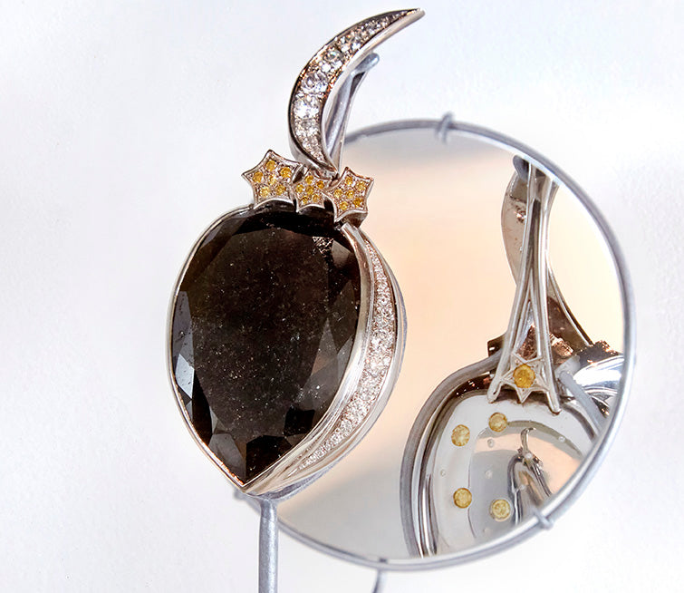 Elegant black diamond pendant with a crescent moon design, accented with yellow diamonds and reflected in a mirror, showcasing intricate craftsmanship in high-end jewelry.