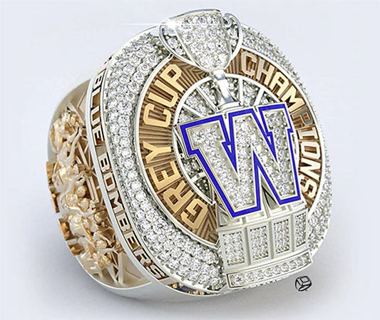 A detailed image of a championship ring featuring the Grey Cup trophy, with a prominent 'W' emblem and diamonds surrounding the design, representing the Winnipeg Blue Bombers as the Grey Cup champions.